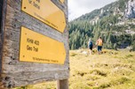 Sign with hiking trails, two hikers in the background