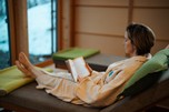 Woman in a bathrobe lies on a lounger and reads