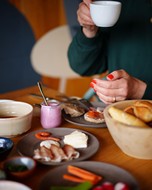 Full breakfast table with a person sitting at it with a cup in their hand