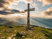 Summit cross on the mountain at dusk, other mountains all around