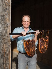 Mann hält eine Stange mit zwei großen, gereiften Stücken Fleisch