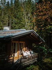 Wooden hut in the forest, two people in bathrobes sitting in front of it