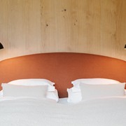Double bed with rust-red headboard in front of a wooden wall
