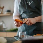 Kochen Sie mit uns Person in Schürze schält eine Karotte