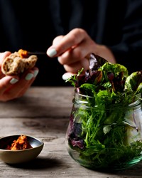 Genießen Sie täglich wechselnde Vitaminschübe Salat im Glas, Aufstrich, dahinter eine Person mit einem Stück Brot