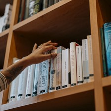 Hand reaches into a bookshelf to pick up a book