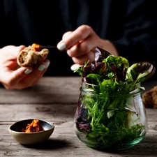 Enjoy daily changing vitamin boosts Salad in a glass, spread, behind it a person with a piece of bread