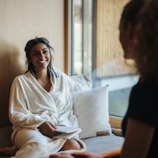 Woman in a bathrobe sits on a windowsill and talks to another person