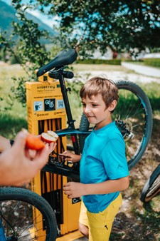 Boy standing in front of bicycle at a repair station and looking at an apple offered to him