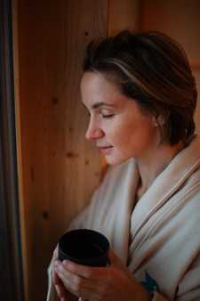 Woman in a bathrobe holds a cup and closes her eyes