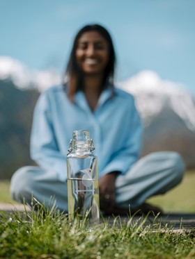 Woman sitting cross-legged in a meadow, a water bottle in front of her