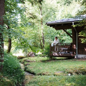 Wooden cabin in the forest, a woman in a bathrobe standing on the veranda.