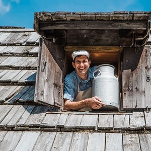 Man with a milk churn looks out of the window of a wooden house