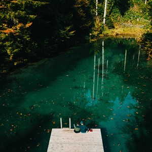 Pond surrounded by trees with a footbridge on which two people are sitting