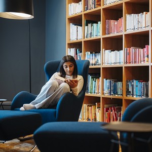 Woman reading in an armchair in front of a bookshelf