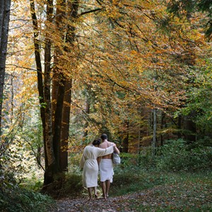 Two people in bathrobes walk through the forest