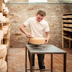 A man brushes a cheese wheel in a room full of cheese wheels.