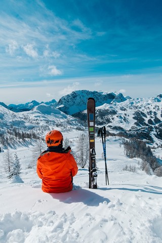 Person with skis next to them sits on a slope and looks into the mountain landscape