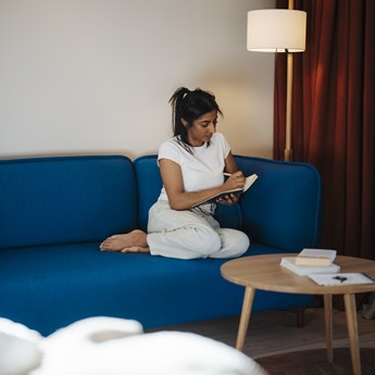 Frau sitzt auf einer Couch und schreibt in ein Notizbuch
