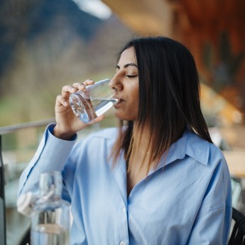Frau sitzt auf einer Terrasse und trinkt Quellwasser 