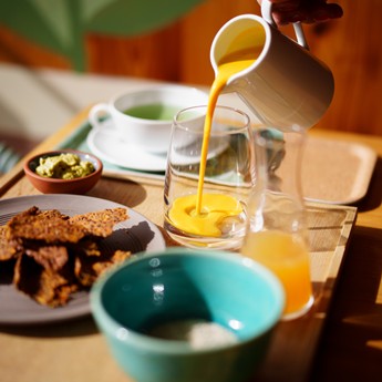 Tablett mit Speisen und Getränken. Orangensaft wird in ein Glas gegossen