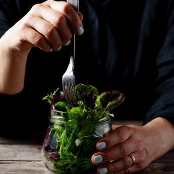 Person sticht mit Gabel in Salat im Glas