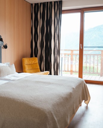 Genießen Sie herrliche Bergblicke Hotelzimmer mit Doppelbett, Stehlampe, Sessel und Fensterfront mit schwarz-weißen Vorhängen.