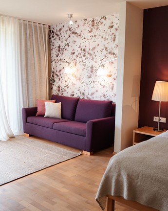 Hotelzimmer mit Sofa, Doppelbett und großer Fensterfront zum Balkon.