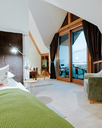 Doppelbett, Sessel und große Glastür zum Balkon im Hotelzimmer