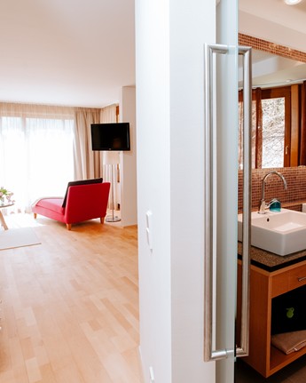 Geräumiges Hotelzimmer mit Bett und Sitzgelegenheit, Blick ins Badezimmer