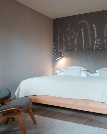 Double bed in a hotel room with a grey headboard and subtle plant wallpaper on the wall behind it.