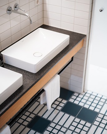 Hotel bathroom with square washbasin and black and white tiles.
