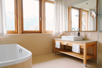Washbasin, mirror and bathtub in bright bathroom with large windows