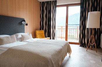 Hotel room with double bed, floor lamp, armchair and window front with black and white curtains.