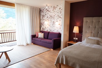 Hotel room with sofa, double bed and large windows facing the balcony.
