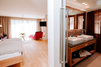 Spacious hotel room with bed and seating area, view of the bathroom
