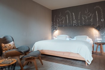 Double bed in a hotel room with a grey headboard and subtle plant wallpaper on the wall behind it.