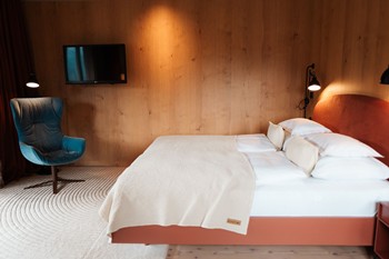 Wood-panelled hotel room with double bed, armchair and television.
