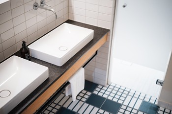 Hotel bathroom with square washbasin and black and white tiles.