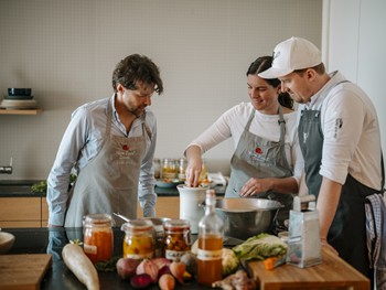 Drei Personen kochen umgeben von Zutaten und Einmachgläsern