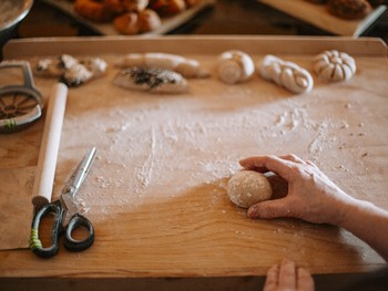Lernen Sie von der Expertin wie Sauerteigbrot gelingt Hand hält Teigball auf gemehltem Holzbrett