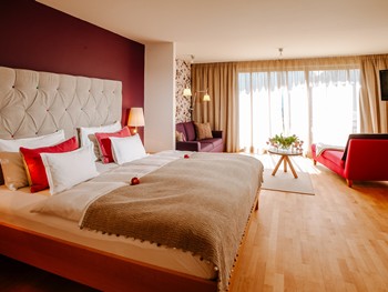 A bright, spacious feel-good place to linger Large hotel room with double bed, seating area and window front