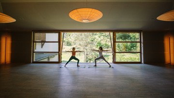 Zwei Frauen machen Yoga in einem Großen Raum mit Öffnung ins Grüne