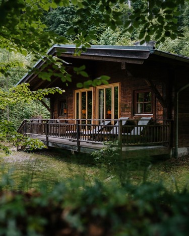 Wooden cabin in the forest with deck chairs on the veranda.