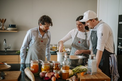 Drei Personen kochen umgeben von Zutaten und Einmachgläsern