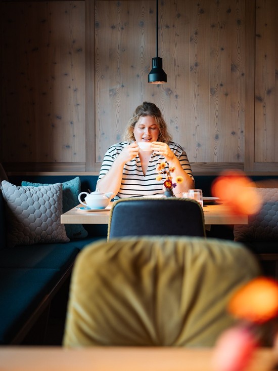 A woman is sitting at a table in a restaurant drinking a cup of tea.