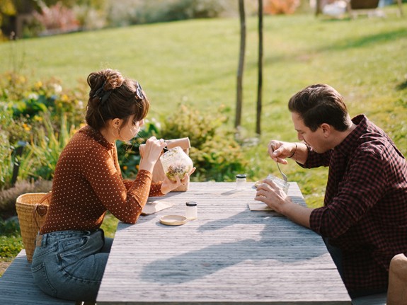 Two people eating at a table in front of a mountainous landscape