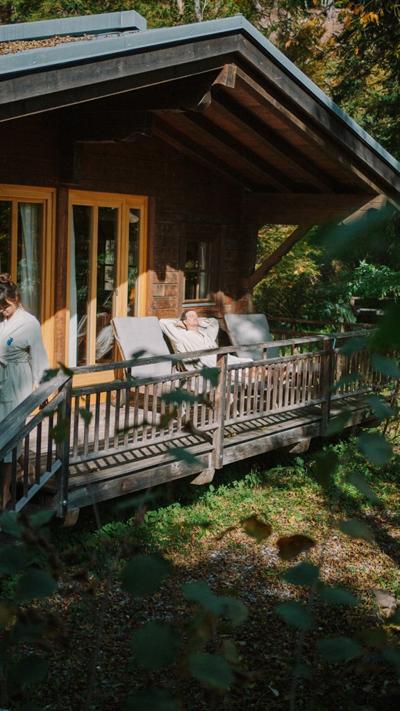 Couple in bathrobes in front of a wooden hut in the forest