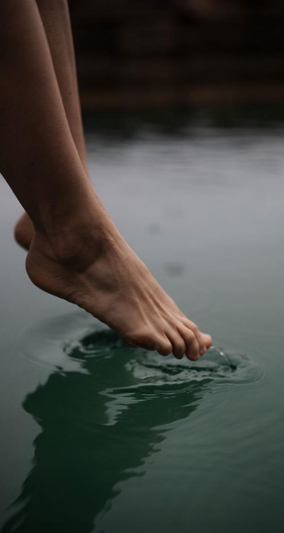 Hanging feet touch calm water