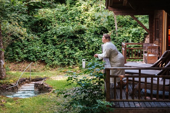 A woman in a bathrobe is standing on the veranda of a wooden hut.